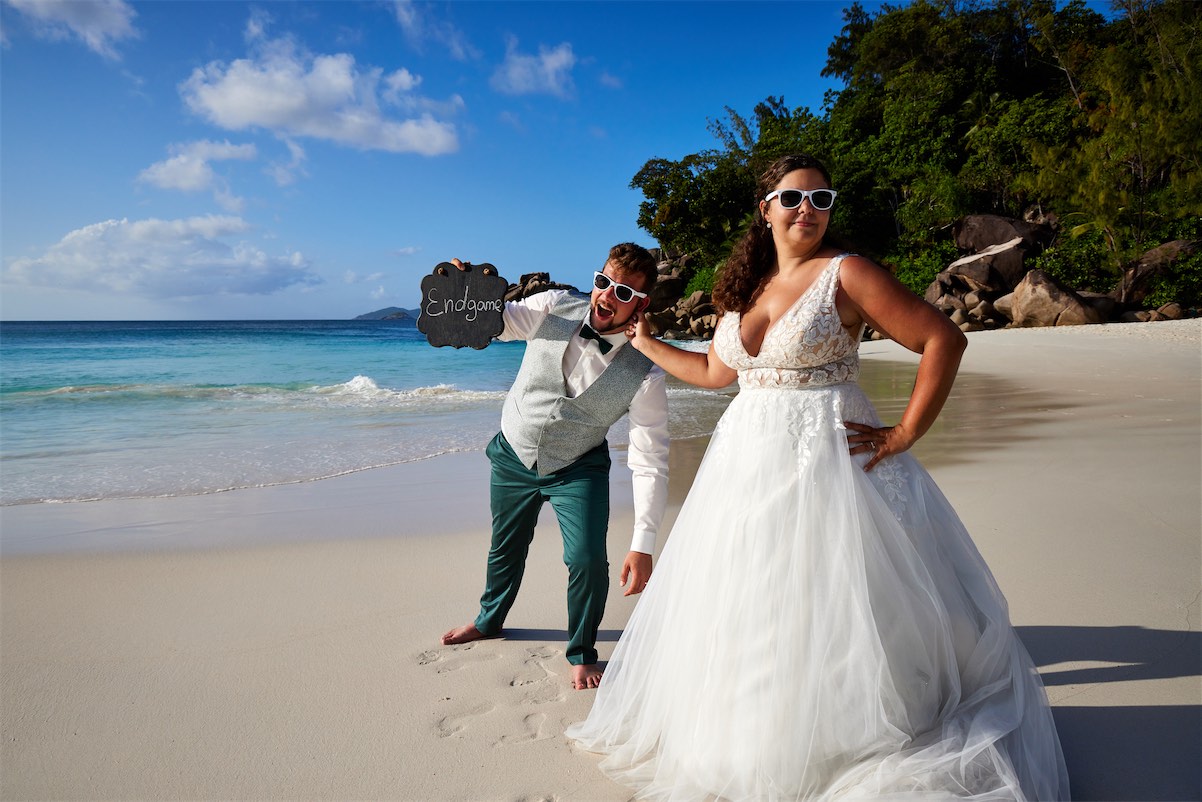 A joyful bride and groom pose for a beach photo, surrounded by sand, celebrating their love on Praslin island.